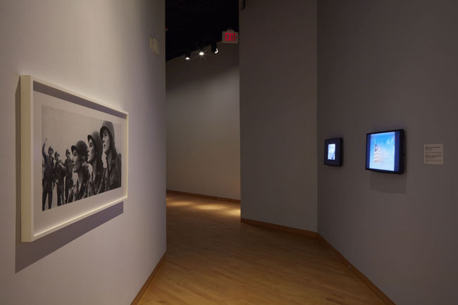 Left to right: Hank Willis Thomas,  The Men Cheered!, 1945/2015, 2015.  Digital chromogenic print.  Museum purchase with funds provided by William and Jane Knapp, 2016, SN11548.7, Collection of The John and Mable Ringling Museum of Art, the State Art Museum of Florida, Florida State University, Sarasota, Florida; Coketails for Dorothy: Monrovia Children’s Birthday Party, 1956. 25 min. black and white video. Produced by Griff Davis, Courtesy of Griffith J. Davis Photographs and Archives; Pepperbird Land – 1952 Liberia (The Country, People, Industry, Leaders), 1952. 23 min. video in color with sound. Narrated by Sidney Poitier, Produced by Griff Davis, Courtesy of Griffith J. Davis Photographs and Archives. Installation view of Still Here: The Griffith J. Davis Photographs and Archives in Context at USF Contemporary Art Museum. Photo: Will Lytch